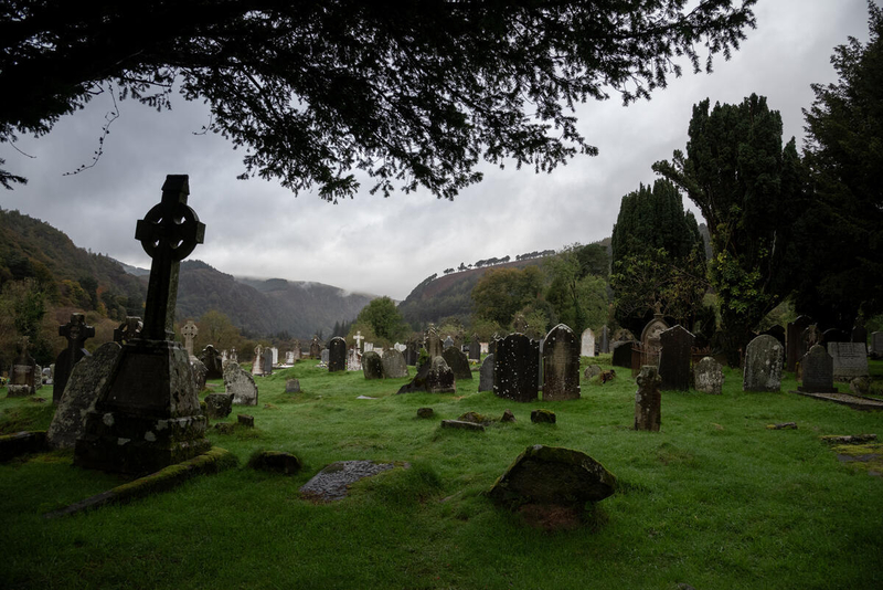Ancient graveyard at Glendalough, County Wicklow, surrounded by misty mountains and lush greenery.